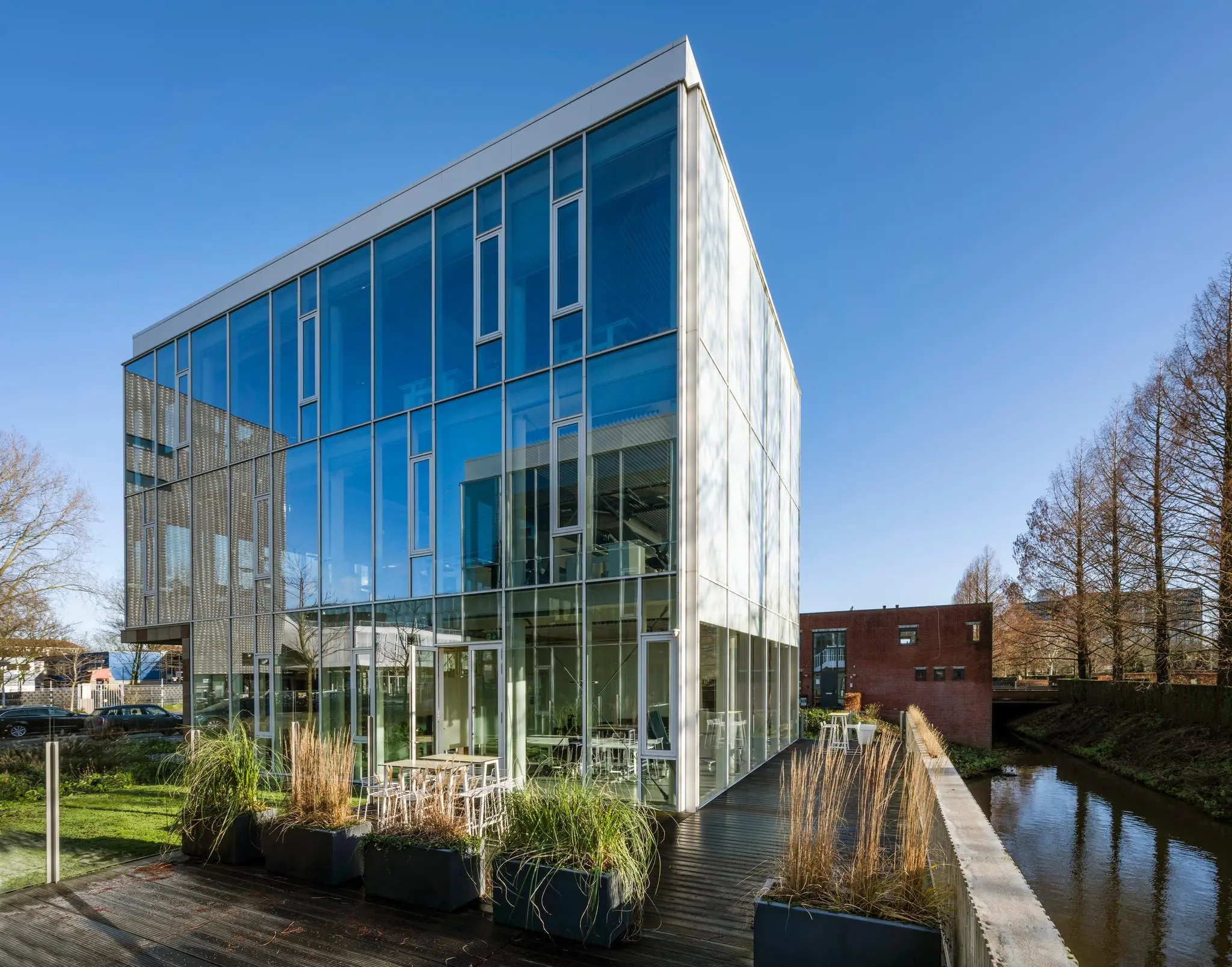 Modern glazen kantoorgebouw aan de Fred. Roeskestraat met terras aan het water en heldere blauwe lucht.